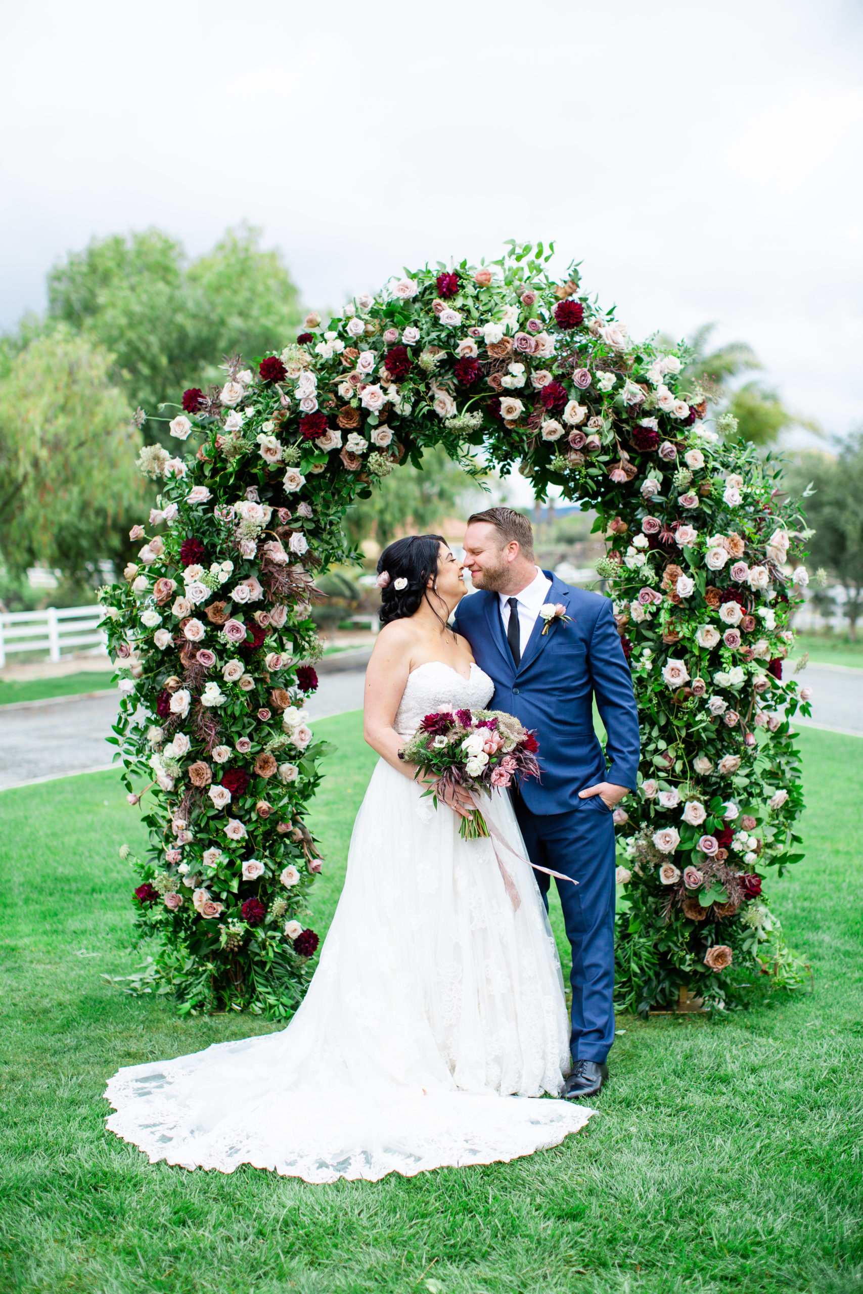 Bride and Groom under a beautiful flowered wedding arch designed by Little Hill Designs