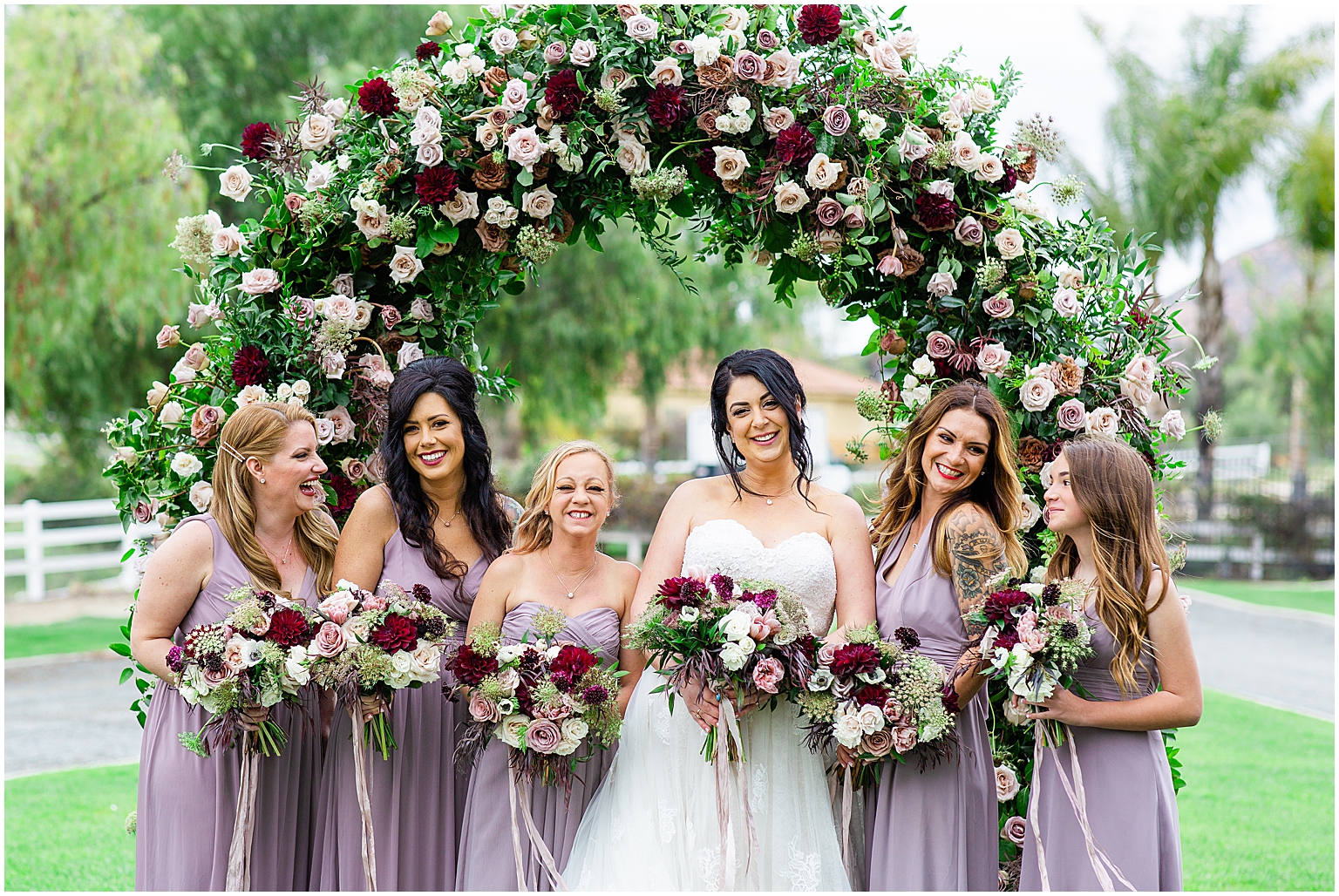 Bride and Bridesmaids together under a beautiful floral arch designed by Little Hill Designs