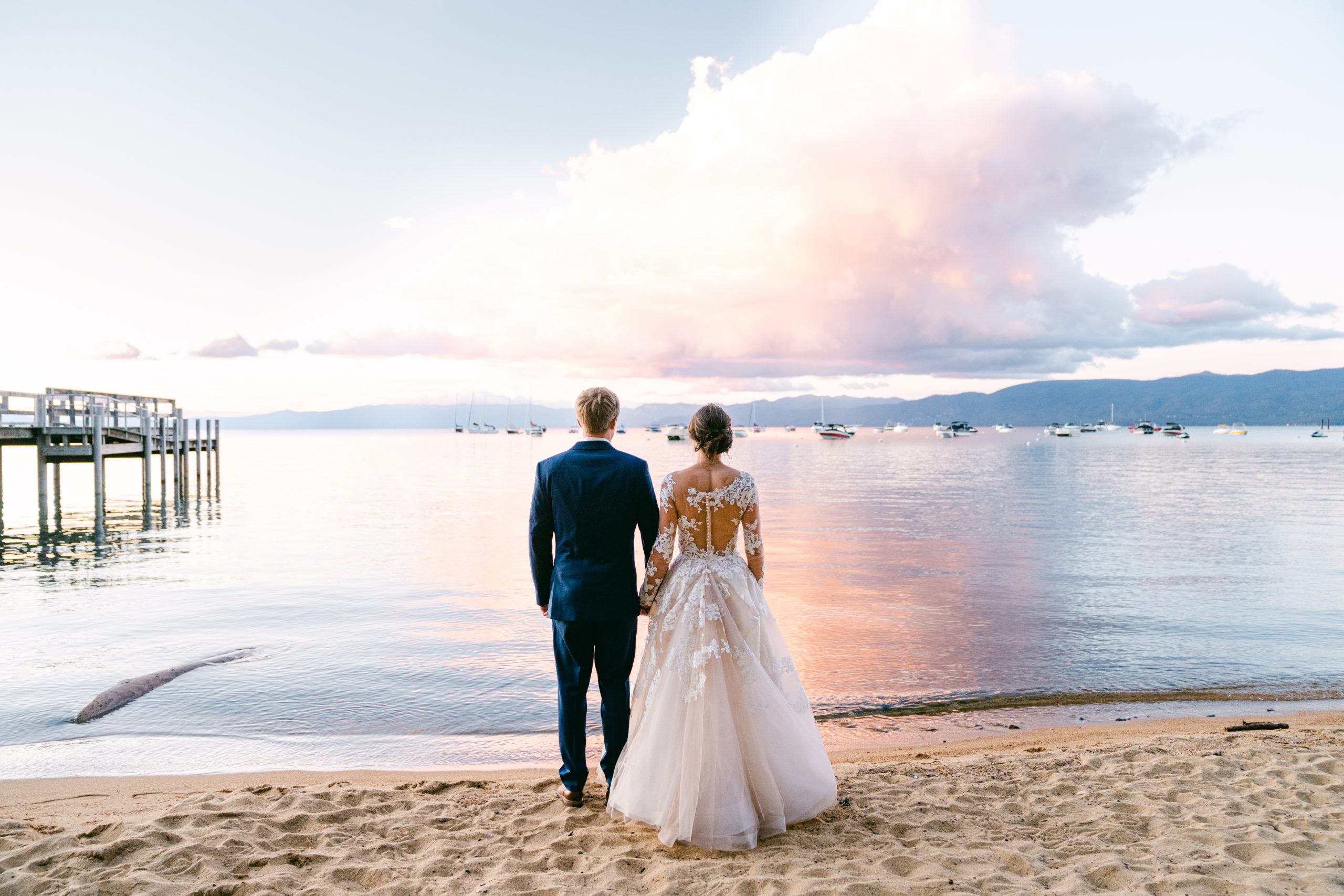 Jake and Emily stand in front of Lake Tahoe with a blue and pink sunset at their destination wedding