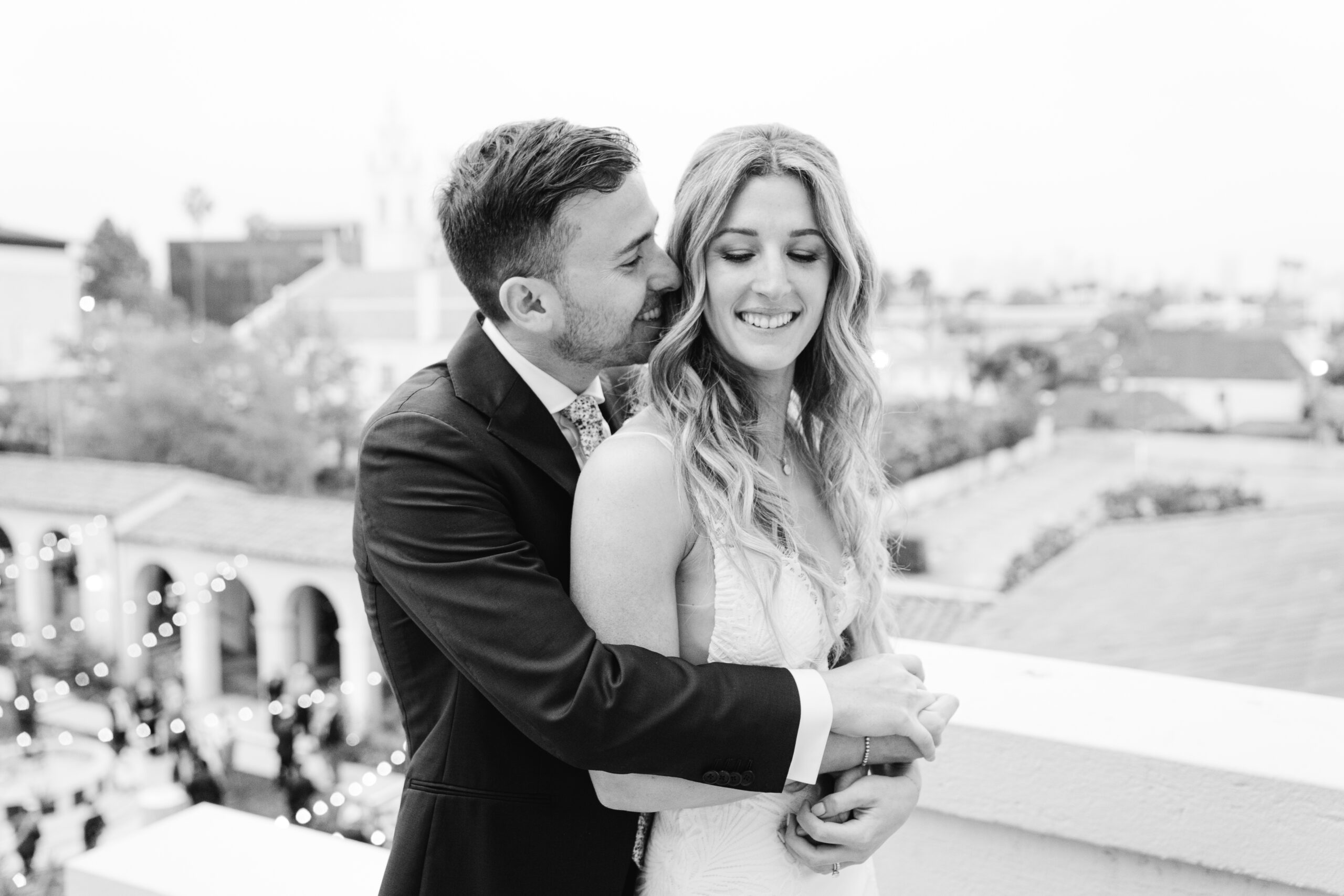 A black and white of the groom embracing his bride. Behind them is the Ebell Los Angeles where their Jewish wedding takes place.
