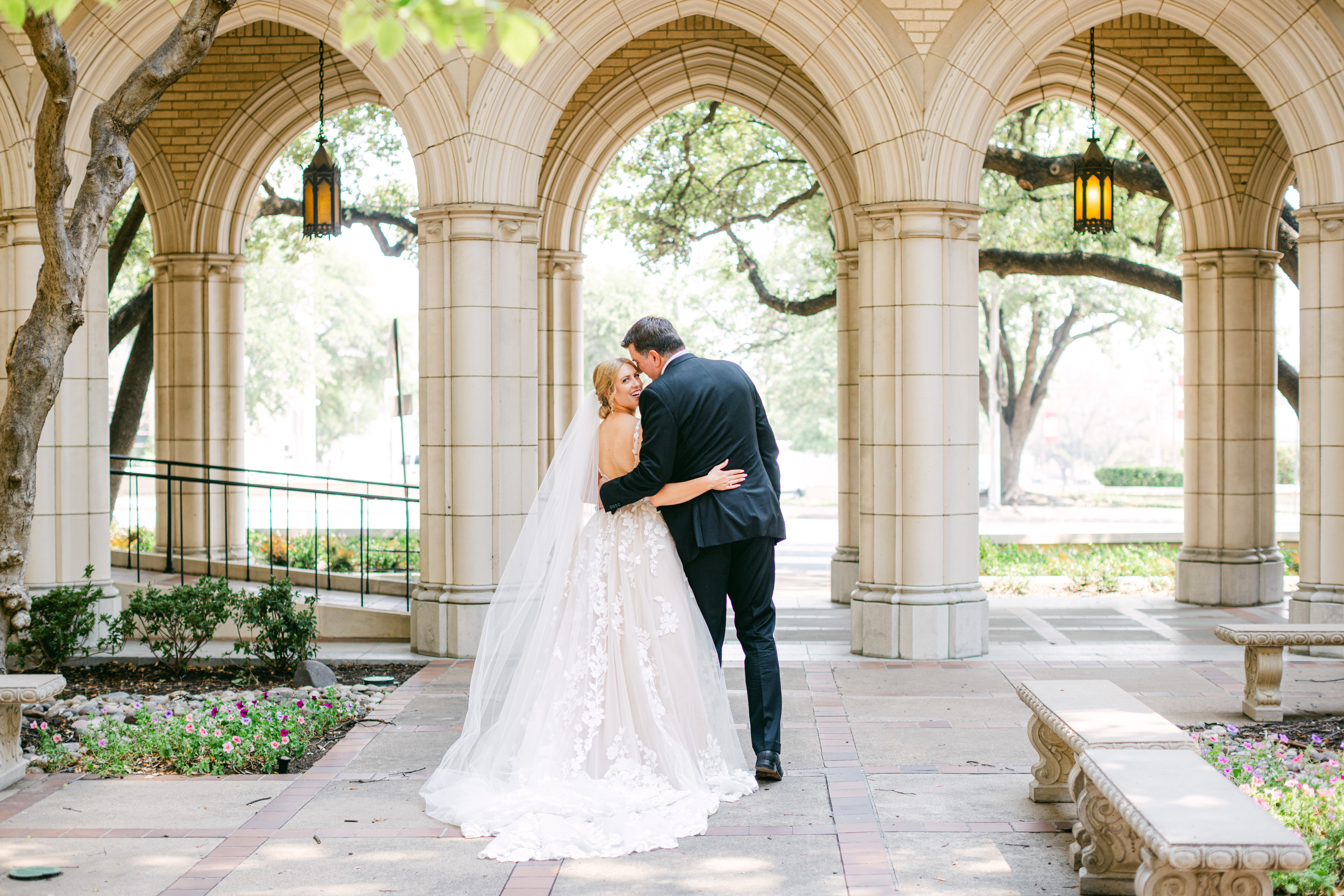 A bride and groom embrace each other and face away, as the bride smiles back at the camera during their Fort Worth, Texas wedding at the historic Texas & Pacific Railway Terminal. Photo by Kate Noelle Photography.